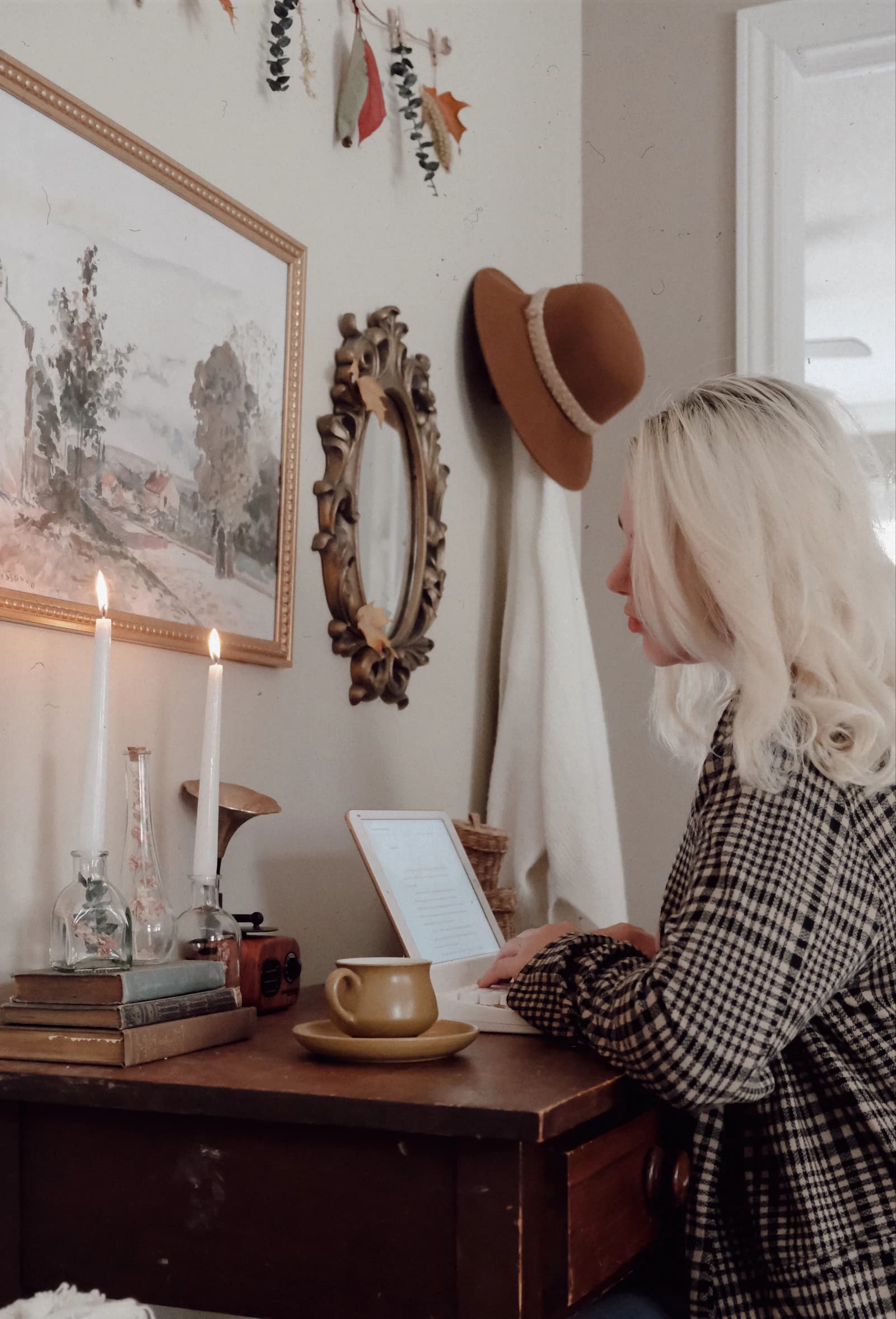 A person working at a laptop beside books and candles at a wooden desk