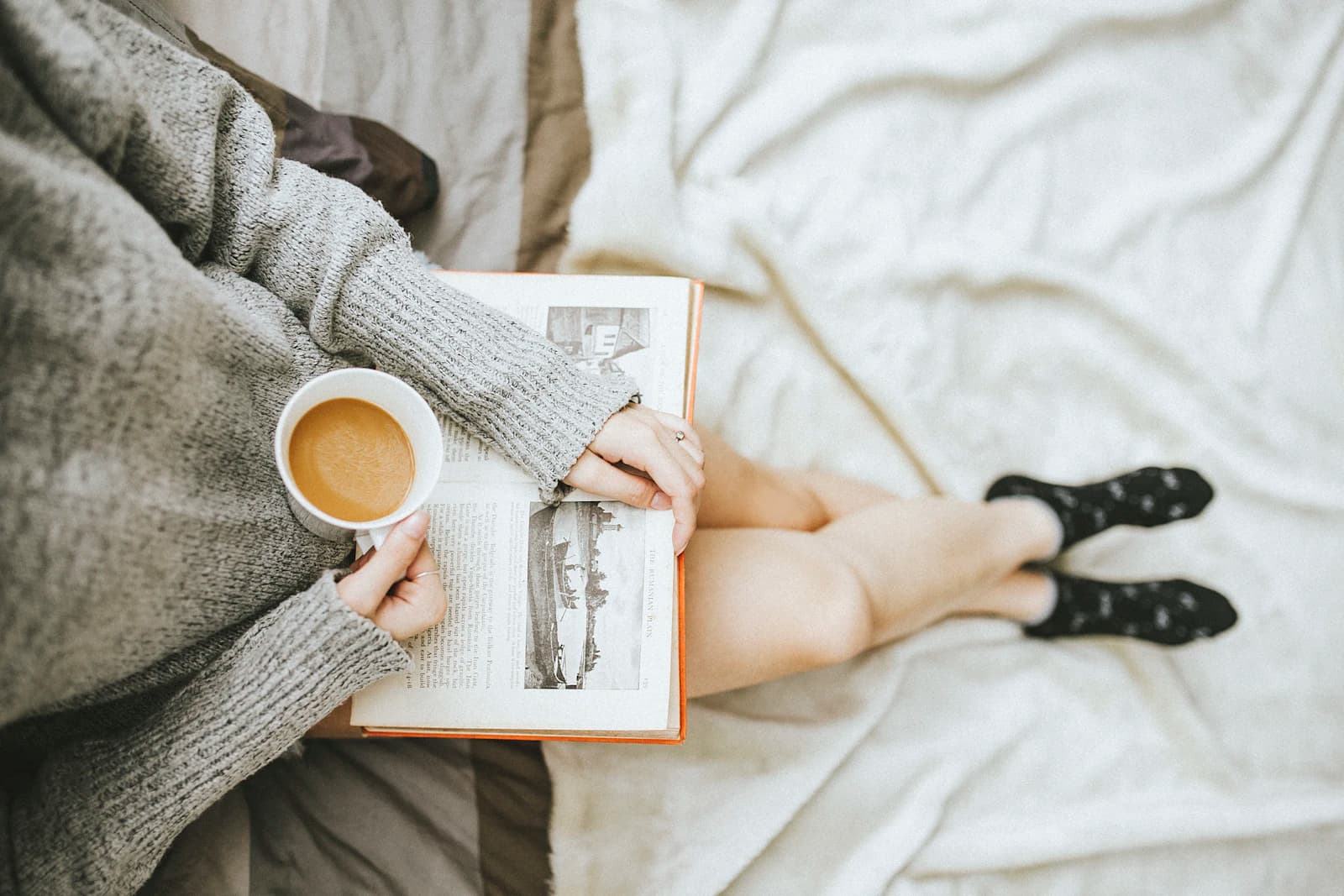 A reader holding an open book and a cup of coffee at home
